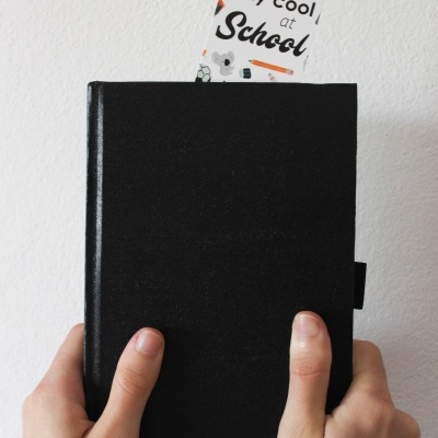 Caderno preto com marcador de página colorido com texto, segurado por duas mãos