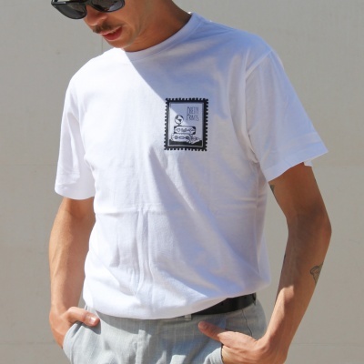 Homem a usar t-shirt branca com estampa preta e branca, calças cinzentas e óculos de sol