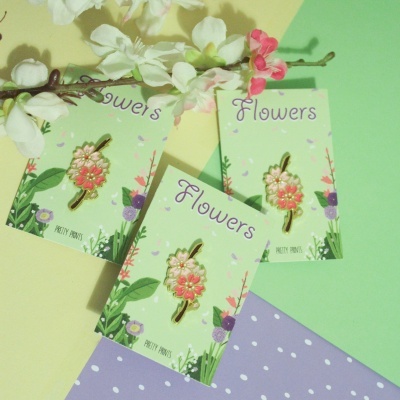 Três pins de flores em cartões verdes com flores ao fundo