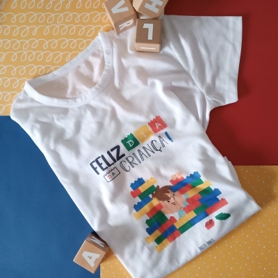 Camisola branca com estampa colorida de blocos e texto FELIZ DIA DA CRIANÇA