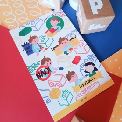 Cartão colorido com desenhos de crianças, peças de Lego e texto em português sobre superfície colorida com blocos de madeira ao fundo