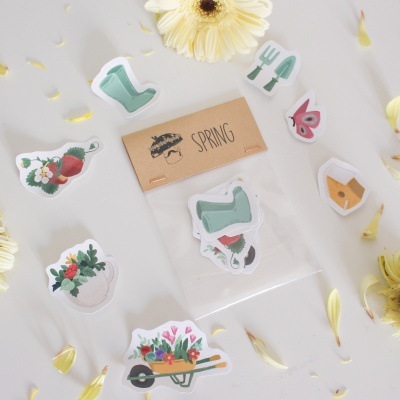 Autocolantes de primavera com temas de jardim e natureza sobre mesa branca e flor amarela.