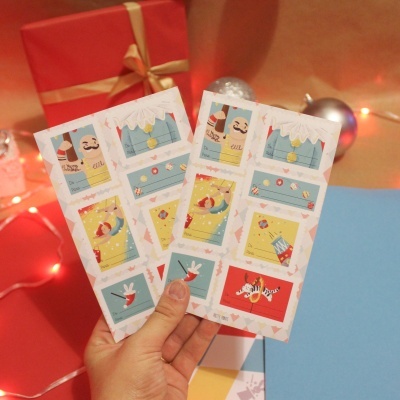 Dois cartões com ilustrações natalícias em mãos, com presente e decorações ao fundo