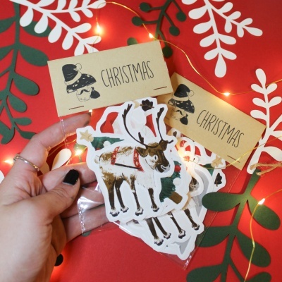 Etiquetas de Natal com design de rena e rótulo CHRISTMAS em saco plástico sobre fundo vermelho com folhas desenhadas e luzes