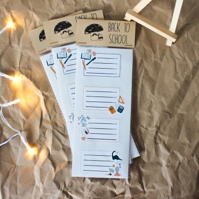 Blocos de notas com embalagem 'BACK TO SCHOOL' sobre papel castanho amassado e luzes decorativas