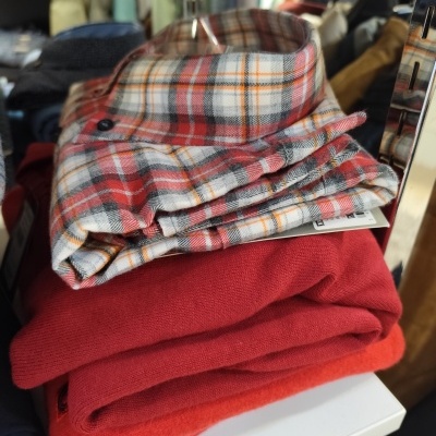 Camisa xadrez vermelha dobrada sobre peças vermelhas numa loja de roupas