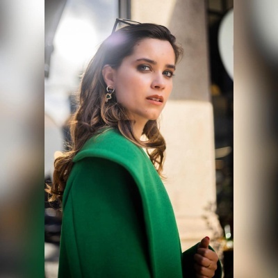 Mulher com casaco verde e brincos dourados em ambiente urbano