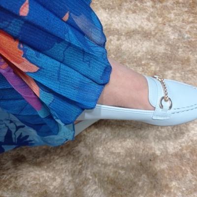 Mocassim branco com detalhe metálico e saia azul colorida sobre tapete bege