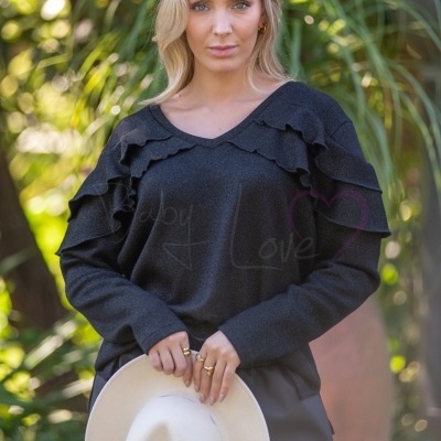 Mulher com camisola preta de folhos a segurar chapéu branco ao ar livre