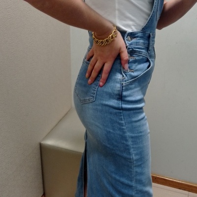 Macacão de ganga azul claro com saia midi e alças, camiseta branca e ténis multicoloridos indoors.
