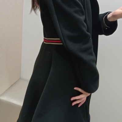 Casaco preto comprido com cinto colorido na cintura, visto de lado