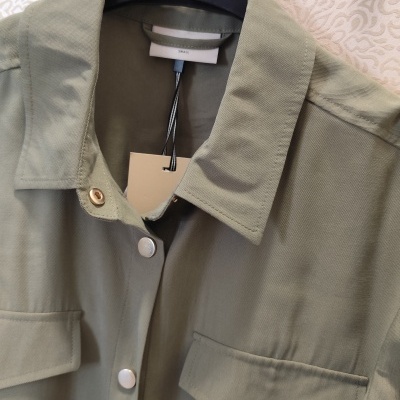 Camisa verde-oliva com botões e bolsos pendurada em cabide preto