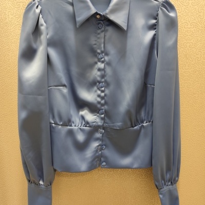 Camisa azul acetinada com botões e gola pendurada em cabide