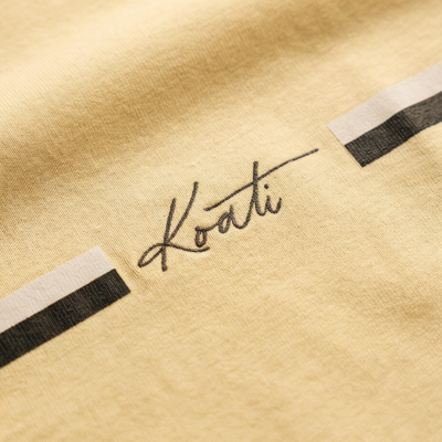 Tecido amarelo com a palavra Koati em preto cursivo e faixas retangulares brancas e pretas