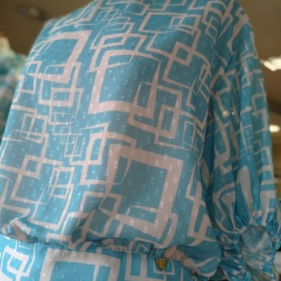 Blusa azul clara com padrão geométrico branco em manequim