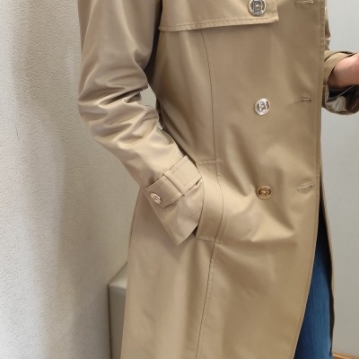 Casaco bege com botões dourados e prateados, calças azuis, sapatos castanhos, tapete bege