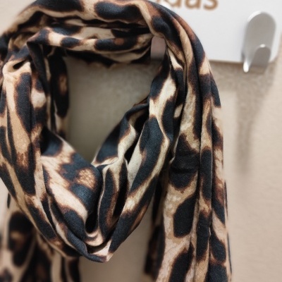 Cachecol com padrão animal print pendurado em suporte branco com a palavra 'Modas'