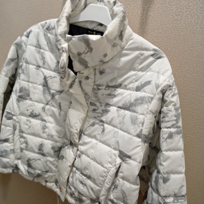 Casaco tipo puffer branco com padrão cinza claro pendurado num cabide branco