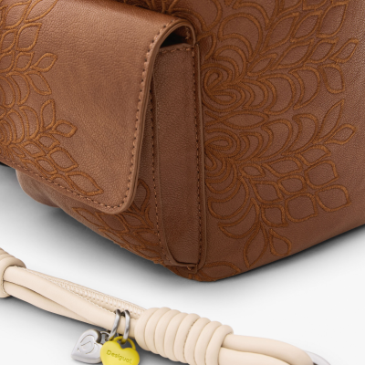 Detalhe de mala castanha com padrão floral e alça bege com pendente amarelo