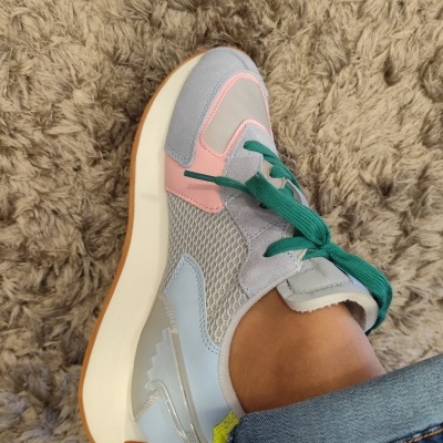 Ténis desportivo colorido com atacadores verdes e sola branca sobre tapete castanho