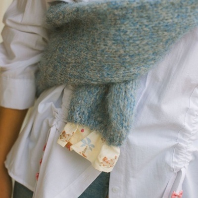 Suéter azul claro de malha grossa sobre camisa branca com laços cor-de-rosa e barra estampada