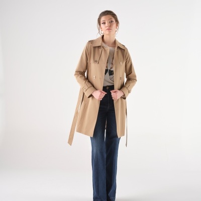 Mulher com casaco trench coat bege e calças azuis largas em fundo branco