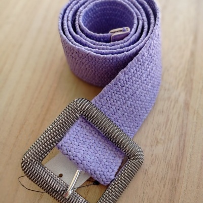 Cinto lilás de tecido trançado com fivela metálica sobre superfície de madeira