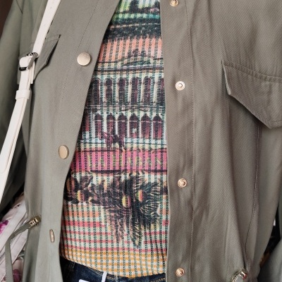 Conjunto com casaco verde oliva, camisola colorida com padrão gráfico e calças de ganga azul