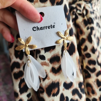 Brincos dourados com folhas brancas translúcidas e cartão Charrete sobre tecido de padrão leopardo