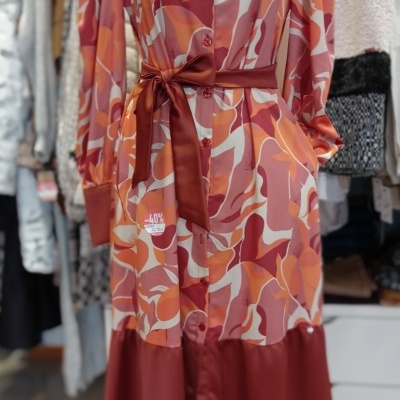 Vestido comprido com padrão abstrato em tons de laranja, vermelho e bege, gola e punhos vermelhos.