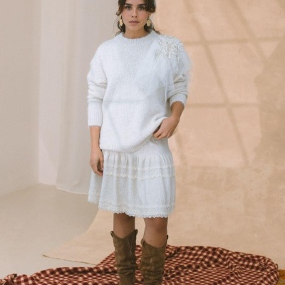 Vestido branco de malha com tule e flores ao ombro e botas castanhas em fundo neutro