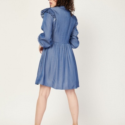 Vestido azul curto com mangas bufantes e babados nos ombros, modelo de costas com sapatos nude