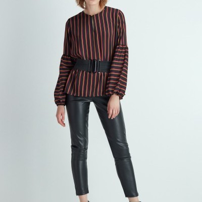 Mulher com blusa riscada e calças de pele preta em fundo branco