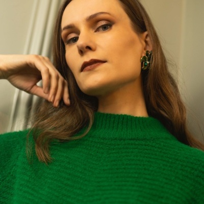 Mulher com suéter verde e brincos dourados com pedras verdes.