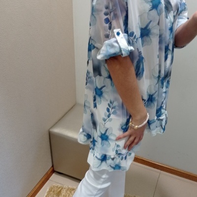 Blusa floral azul e branca com calças brancas e sapatos de salto em ambiente interior