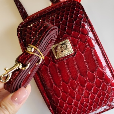 Bolsa de mão vermelha com padrão pele de crocodilo e etiqueta vermelha com cavalo.