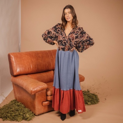 Vestido comprido com estampa floral e saia azul e vermelha, mulher junto a sofá de couro castanho