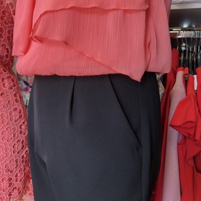 Roupa feminina com blusa coral texturizada e calças pretas lisas expostas em loja de roupas