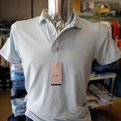 Polo azul claro manga curta com etiqueta rosa C.117 em manequim numa loja