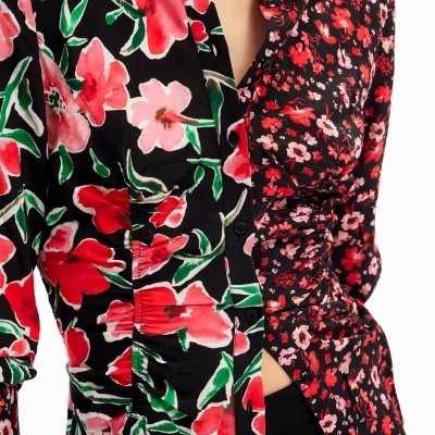 Camisa de manga comprida com padrão floral dividido em duas partes distintas, uma com flores maiores e outra com flores pequenas, ambas em tons vermelhos, rosas e verdes sobre fundo preto.
