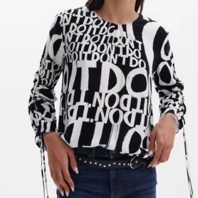 Modelo a usar camisola preta e branca com padrão de texto e jeans azuis.