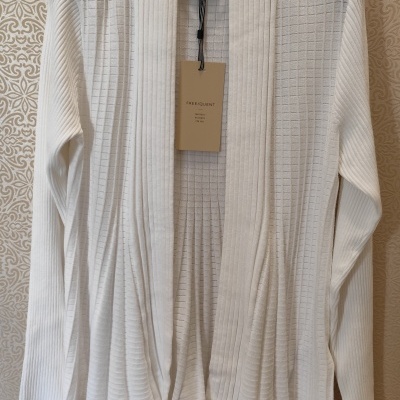 Camisola branca de malha com gola aberta pendurada num cabide preto contra papel de parede bege decorativo