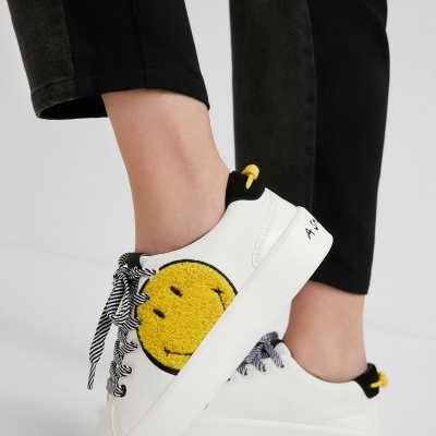 Ténis brancos com smiley amarelo e atacadores às riscas pretas e brancas