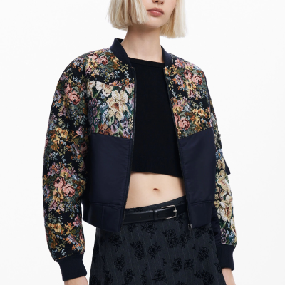 Casaco bomber floral com partes lisas e saia preta com padrão floral, usado por mulher de cabelo loiro.