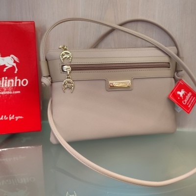 Mala de ombro bege Cavalinho junto a caixa vermelha da marca