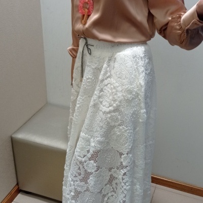 Conjunto feminino com camisa rosa acetinada, saia branca de renda floral e sandálias bege.