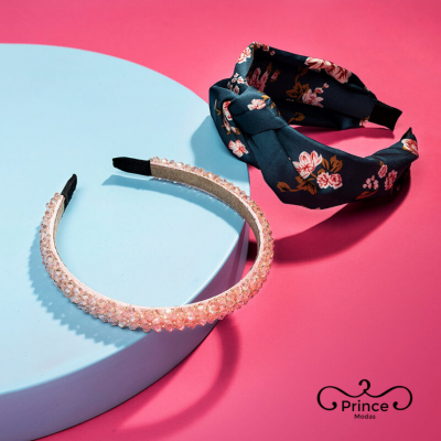 Duas tiaras, uma transparente com contas e outra de tecido floral preto, sobre fundo rosa com logótipo Prince Modas.