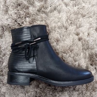 Bota preta de cano curto com textura escamas e laço decorativo num tapete bege