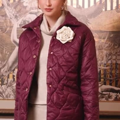 Mulher com casaco acolchoado roxo e flor branca, roupa bege e botas castanhas