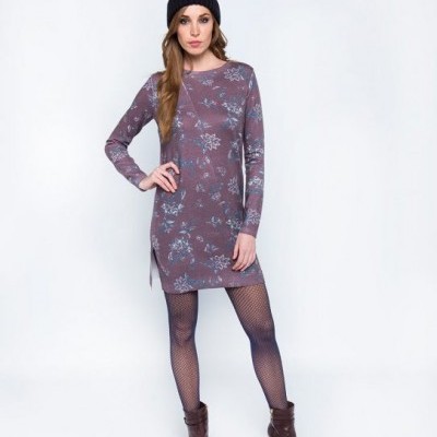 Mulher com vestido floral roxo, meia-calça de rede preta, botas castanhas e gorro preto com pompom